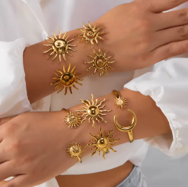 Gold sun-shaped jewelry on a person's wrist against a white background