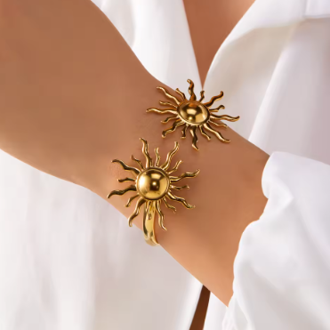Gold sun-shaped cuff bracelets on a person's wrist against a white background