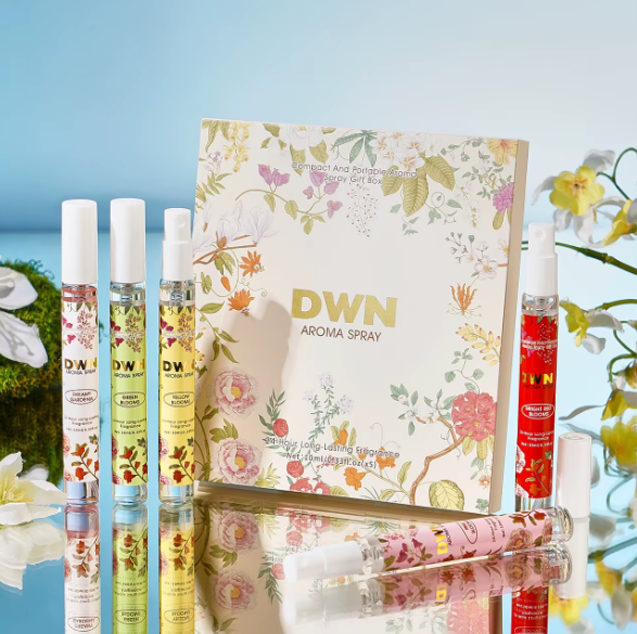 Set of DWN aroma spray bottles with a floral-themed packaging box on a reflective surface with flowers in the background.