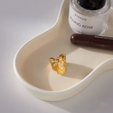 Gold ring on a white dish with Byredo perfume bottle and makeup item in the background