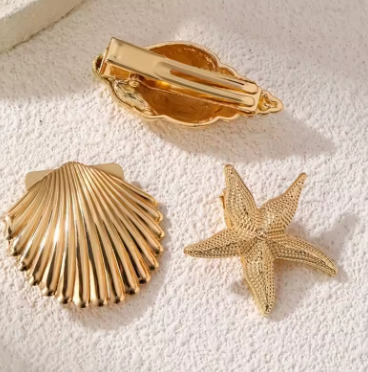 Gold shell and starfish-shaped hair clips on a textured white surface