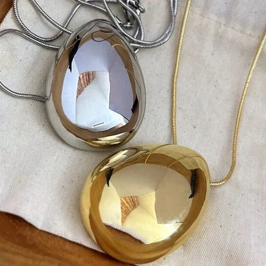 Two gold pendants on a wooden surface with a neutral background