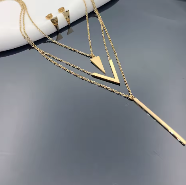 Gold necklace with geometric pendants on a reflective surface