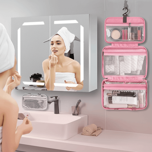 Woman applying makeup in front of a mirror with a pink toiletry bag open on a bathroom counter.