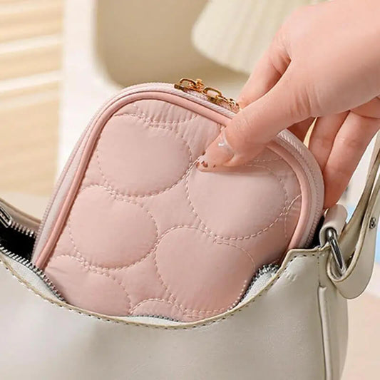 Hand holding a pink quilted pouch with a gold zipper against a neutral background
