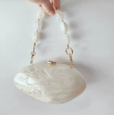 Handbag with shell design and gold accents held by a hand against a white background
