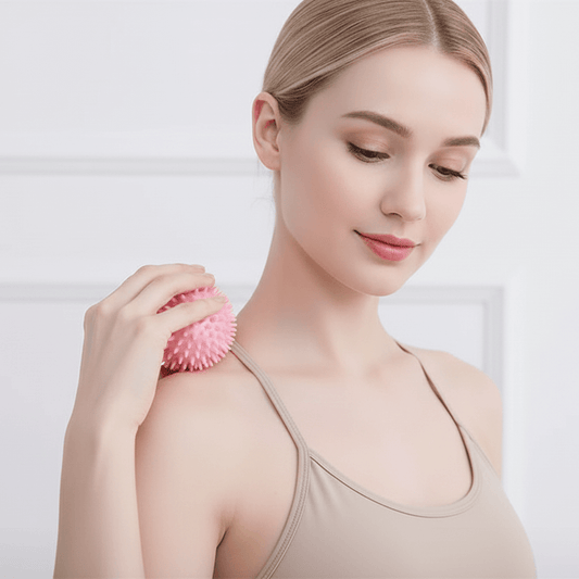 Woman using a pink massage ball on her shoulder against a light background