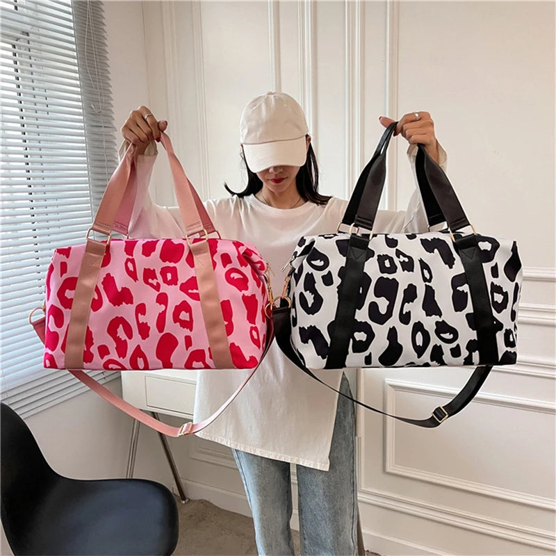 Person holding two leopard print duffel bags, one pink and one black and white, in a room.