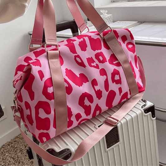 Pink leopard print duffel bag with brown straps on a suitcase.