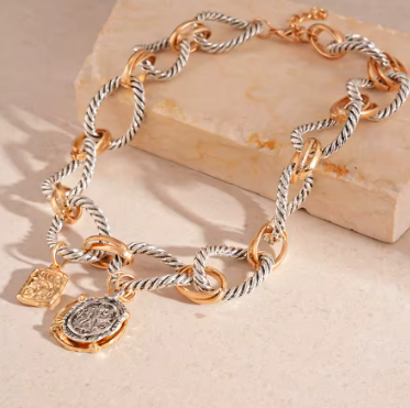 Gold and silver chain bracelet with charms on a wooden block