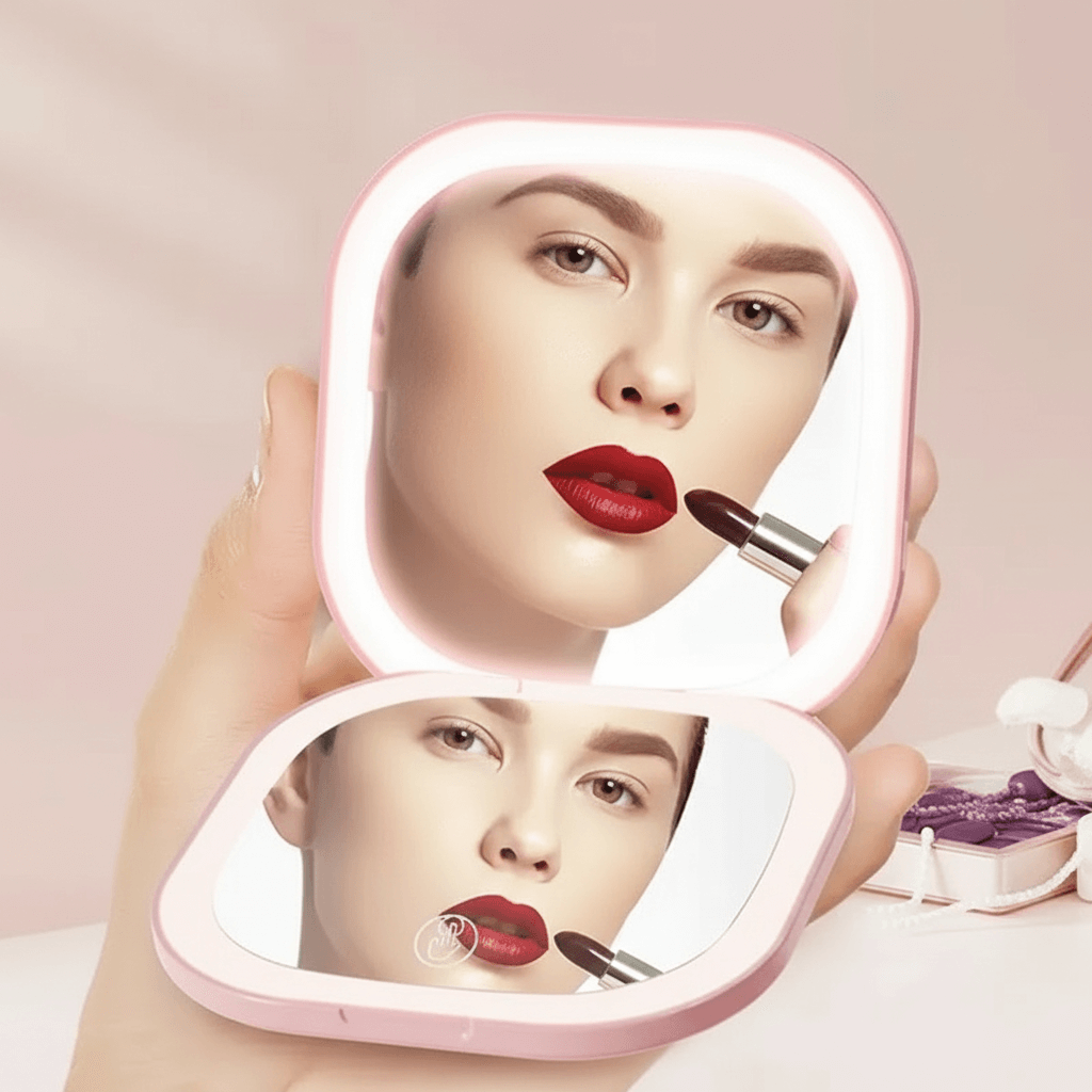 Person applying lipstick in front of a light-up makeup mirror with a pink border.